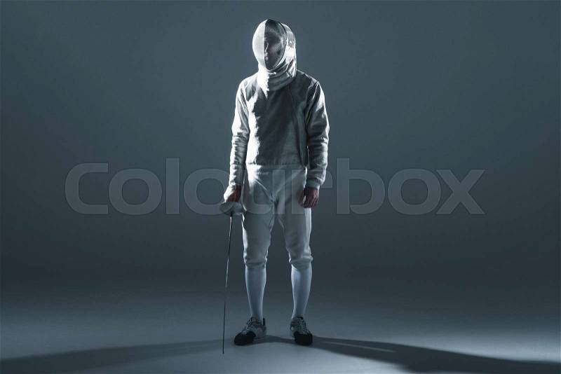 Professional fencer in fencing mask with rapier standing on grey, stock photo