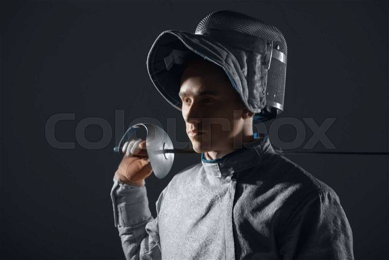 Portrait of professional fencer in fencing mask with rapier on grey, stock photo