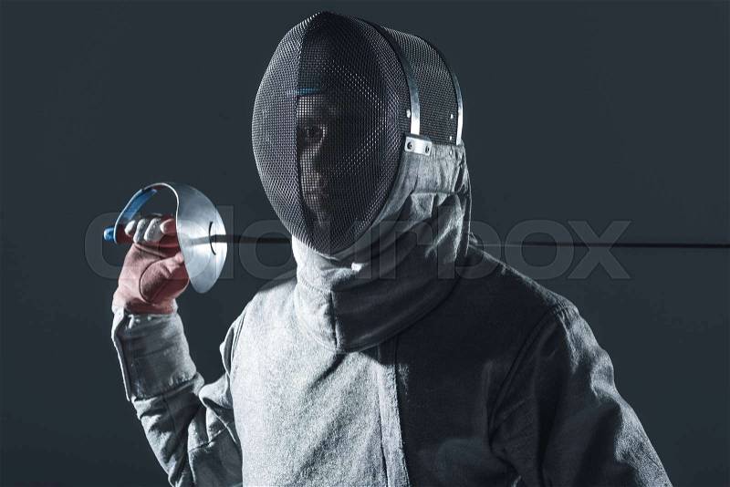 Portrait of professional fencer in fencing mask with rapier on grey, stock photo