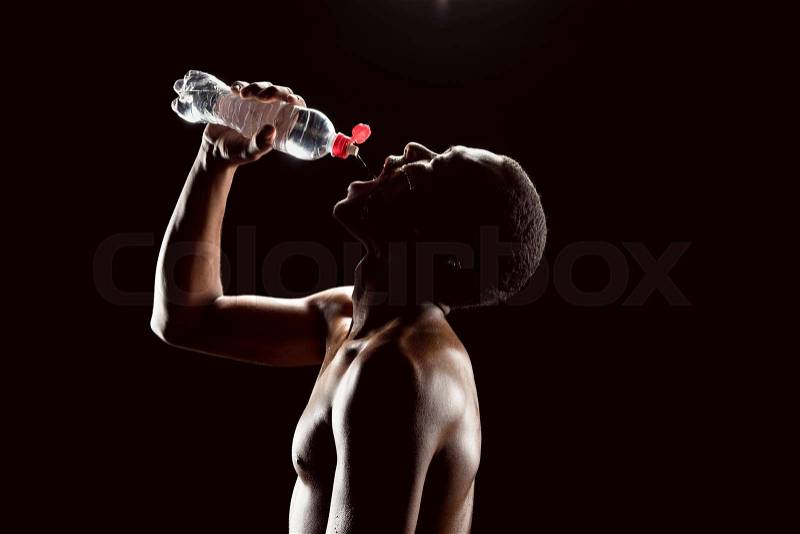 Side view of sporty african man drinking water after training on black, stock photo