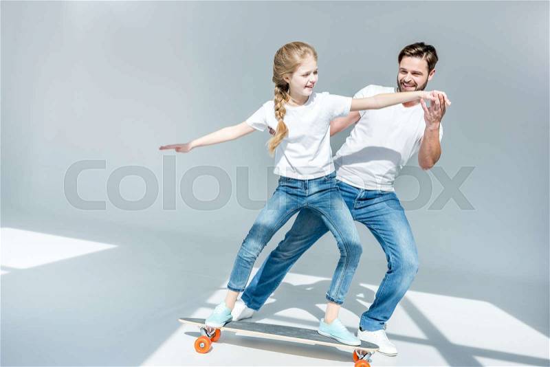 Happy father teaching cute little daughter riding skateboard, stock photo