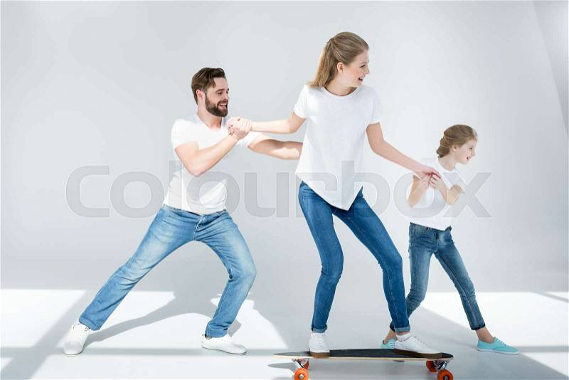 Happy father and daughter helping young woman riding skateboard, stock photo