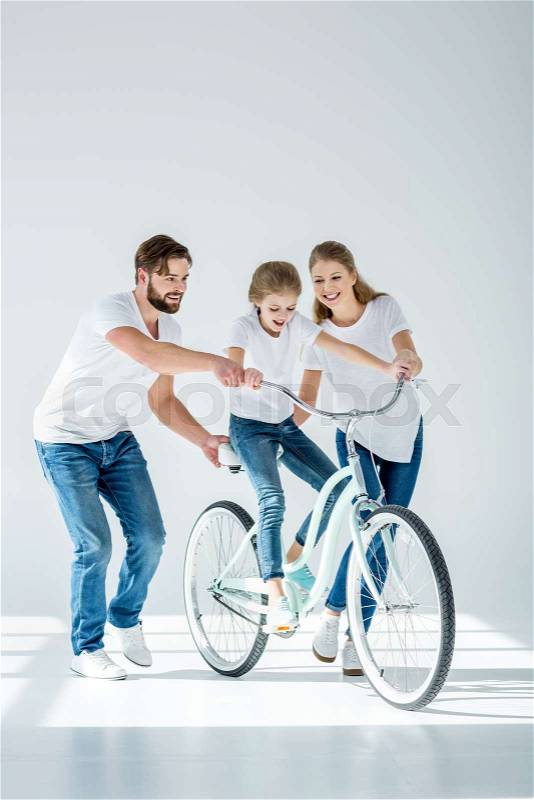 Happy parents teaching cute little daughter riding bicycle, stock photo