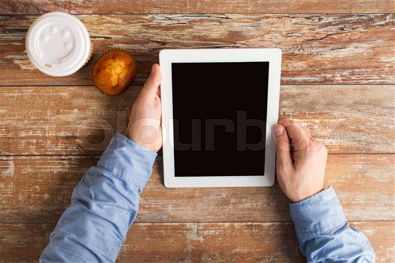 Business, people and technology concept - businessman hands with tablet pc computer, coffee cup and muffin sitting at wooden table, stock photo
