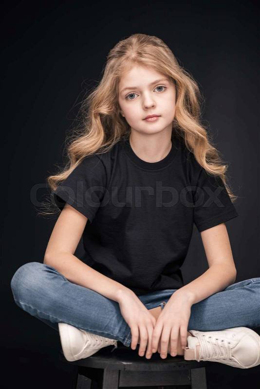 Adorable little girl sitting on stool looking at camera on black, stock photo