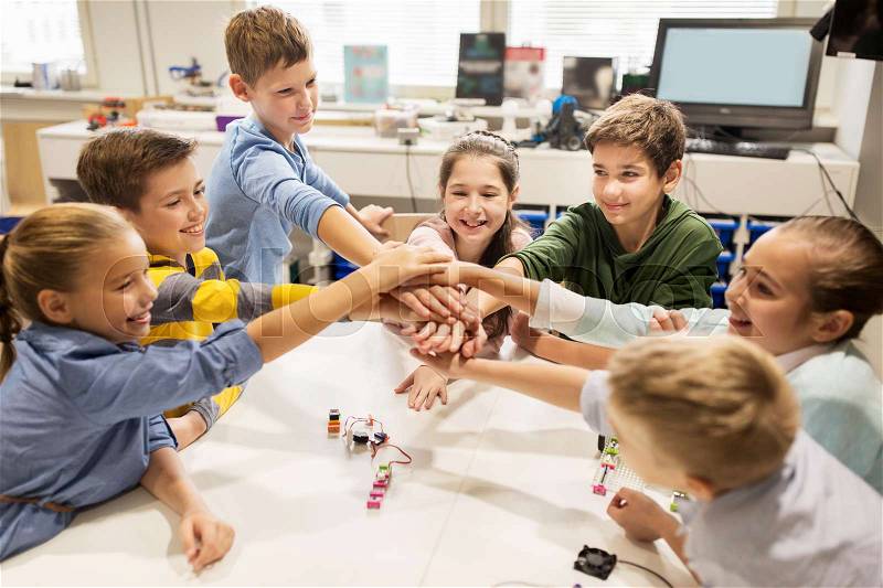 Education, children, technology, science and people concept - group of happy kids building robots l at robotics lesson and holding hands together, stock photo