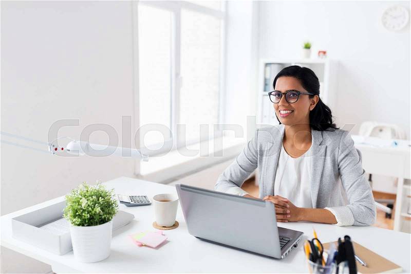 Business, people, work and technology concept - happy smiling businesswoman with laptop computer at office, stock photo