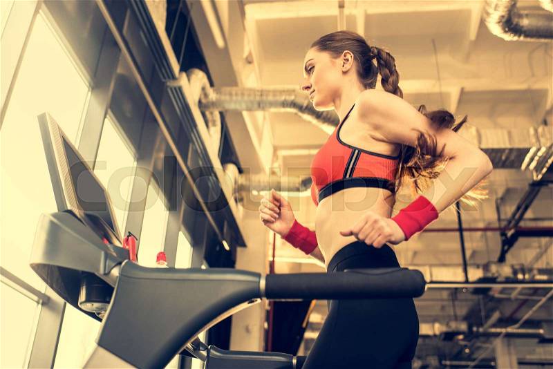 Low angle view of young sporty woman exercising on treadmill in gym, stock photo
