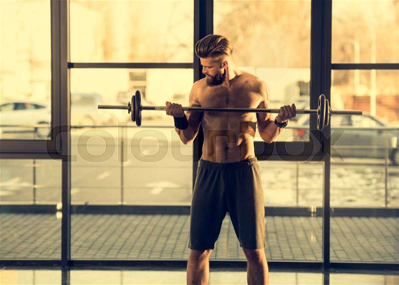 Front view of bearded sportsman training with dumbbell in sports center, stock photo