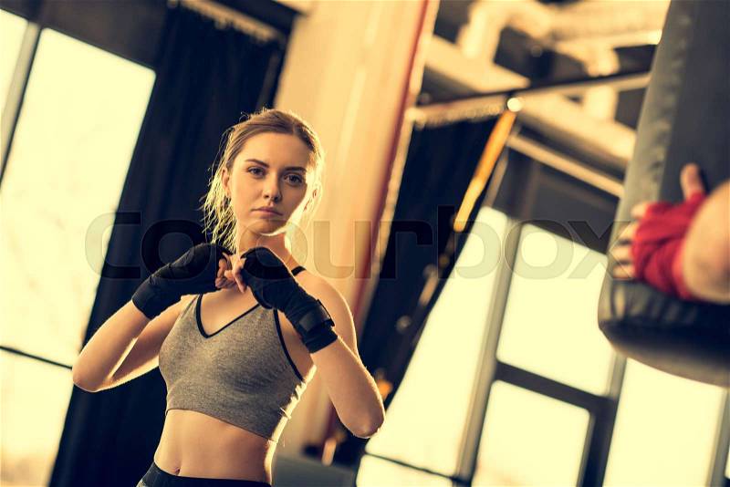 Young attractive sportswoman with punching bag in sports center, stock photo