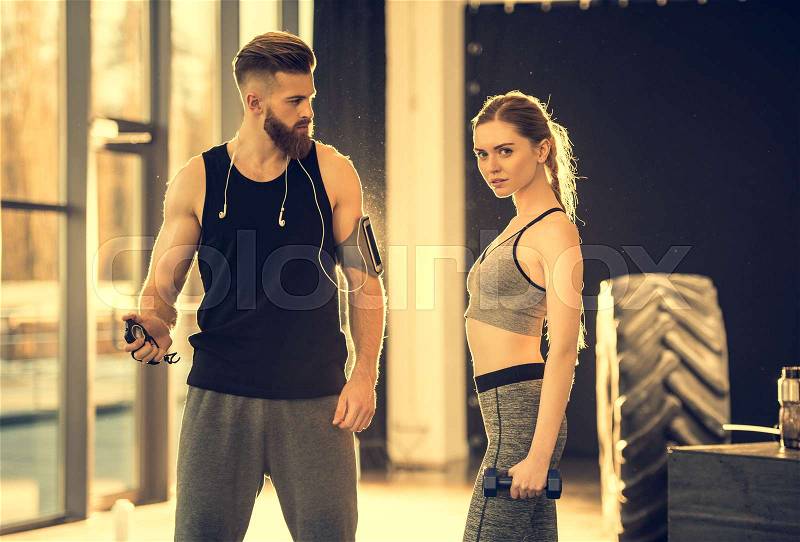 Young sportsman and sportswoman with dumbbell and timer standing in sports center, stock photo