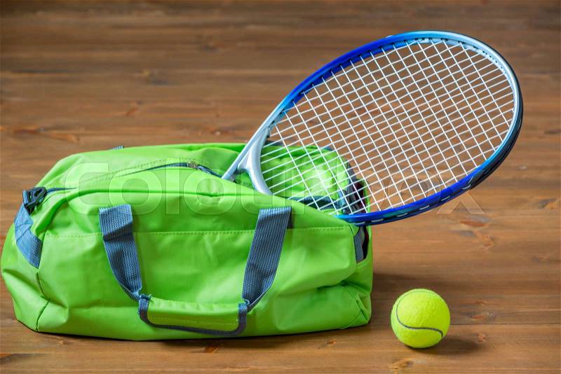 A tennis racket sticks out of a green sports bag, objects on the floor, stock photo