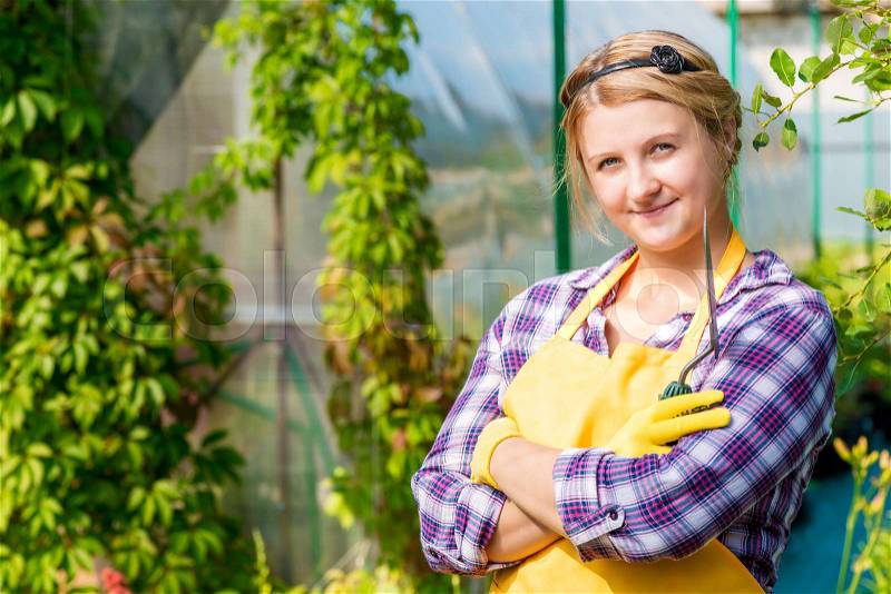 Young girl in apron with gardener tools in a greenhouse, stock photo