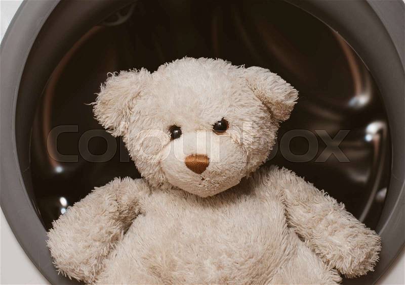 Plush bear sitting on washing machine, stock photo