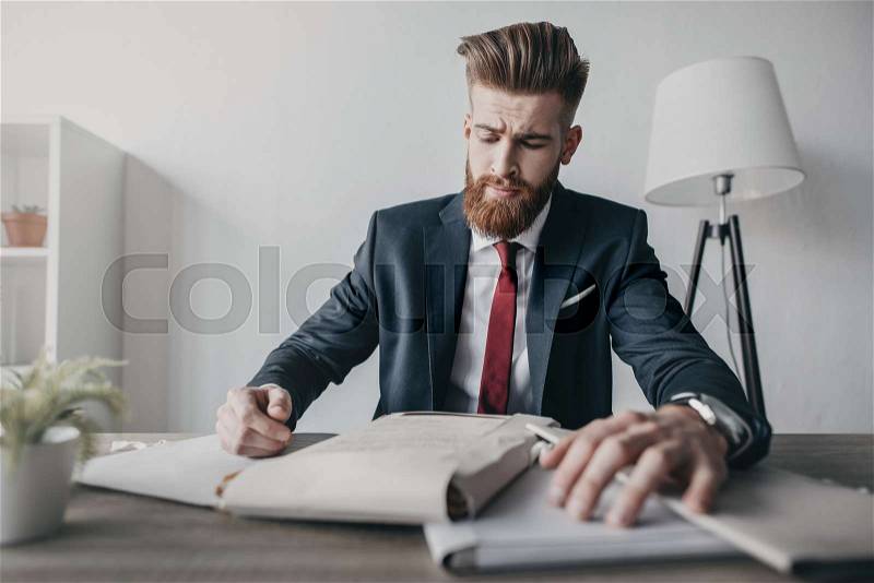 Young businessman with documents and folders sitting at table in office, stock photo