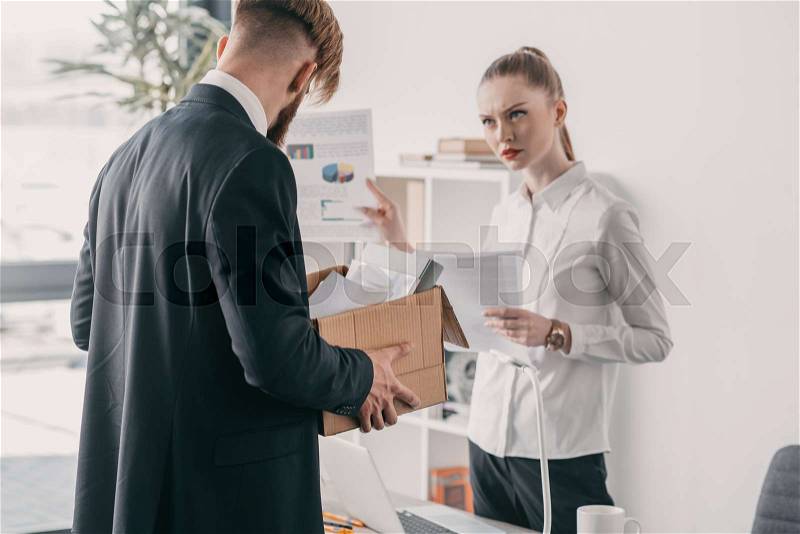 Young upset fired businessman with cardboard box and businesswoman in office, stock photo