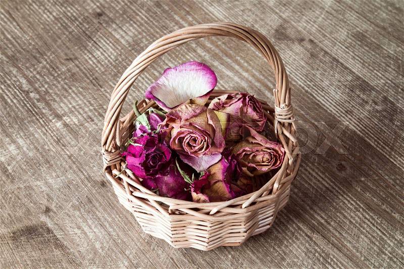 Buds of dry roses in wicker basket on wooden background, stock photo