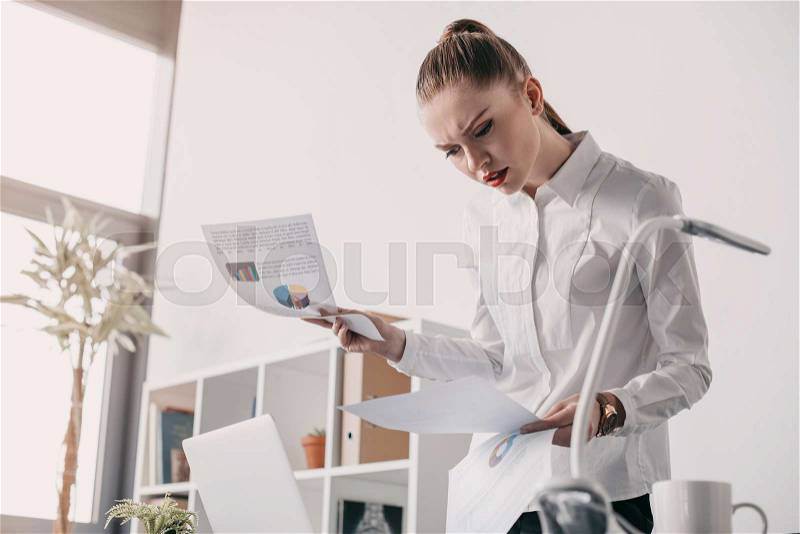 Young concentrated businesswoman reading business documents in office , stock photo