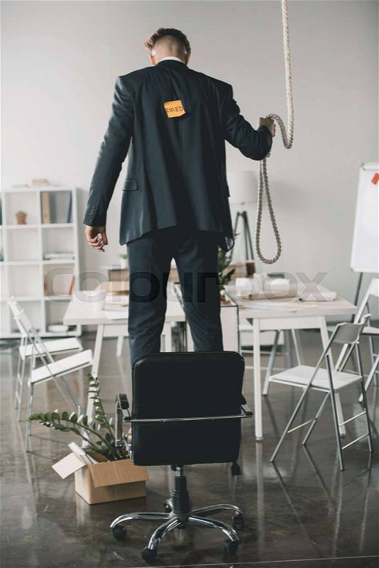 Back view of fired businessman standing on chair and trying to hang himself in office, stock photo