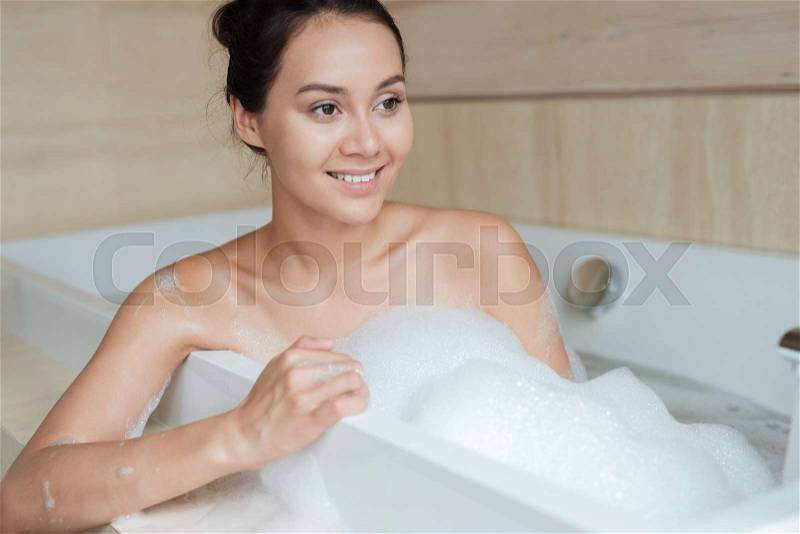 Portrait of a smiling asian woman enjoying bubble bath at home, stock photo