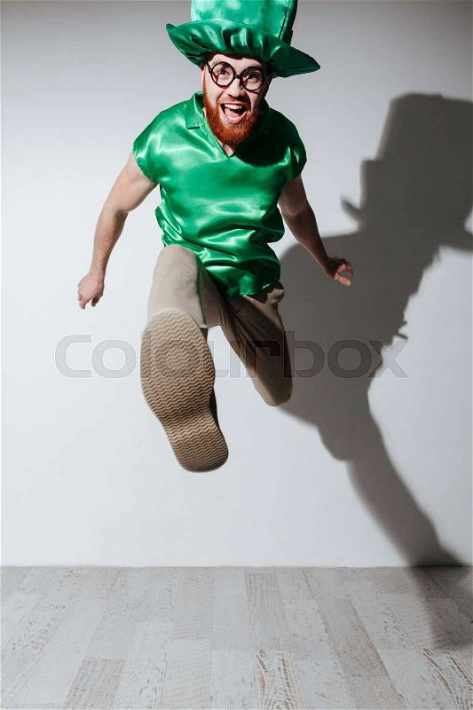 Vertical image of happy man in st.patriks costume and eyeglasses which jumping in studio. Isolated gray background, stock photo
