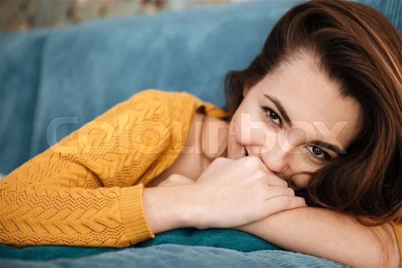 Close up portrait of a pretty shy girl looking at camera while laying on a couch indoors, stock photo