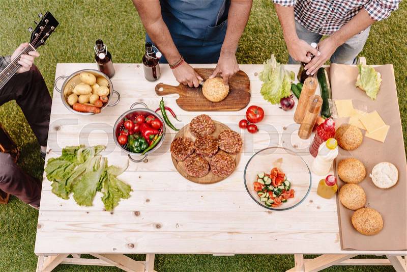 Elevated cropped view of friends making burgers on table outdoors, stock photo
