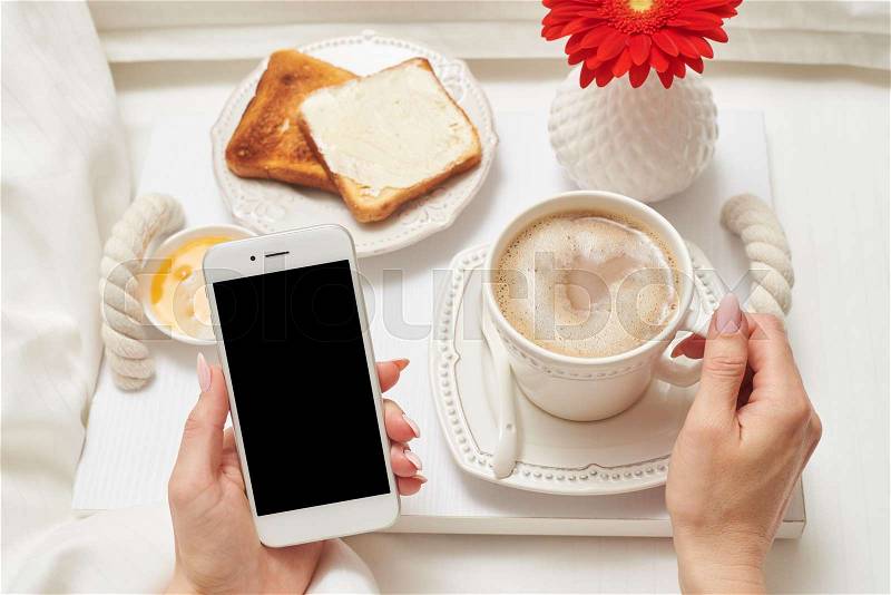 Close-up shot of female hand holding telephone in hand while having breakfast in the morning, stock photo