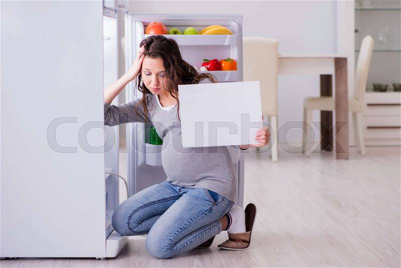 Pregnant woman near fridge with blank message, stock photo