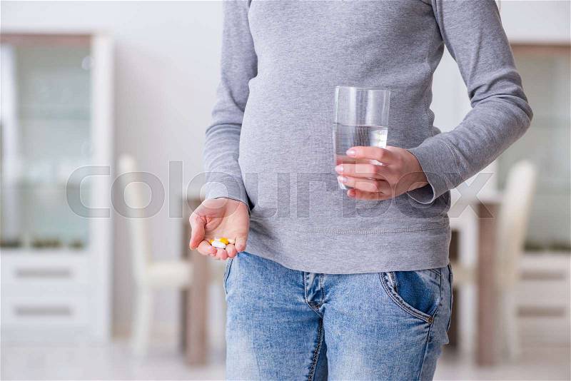 Pregnant woman taking pills during pregnancy, stock photo