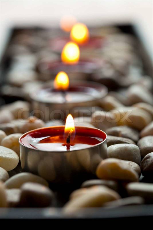Close-up of red tea-light candles on pebbles, stock photo