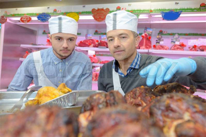 Butcher showing apprentice cooked meats, stock photo