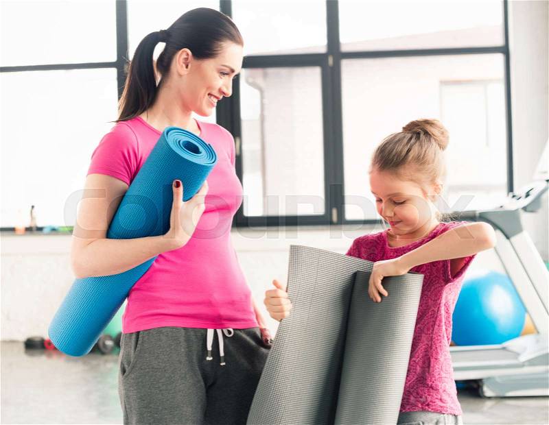 Mother and daughter in pink shirts holding yoga mats in gym, stock photo