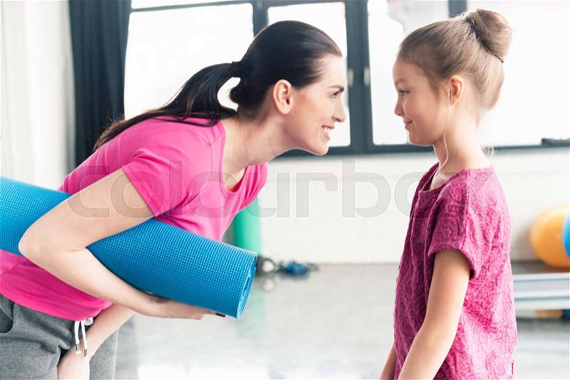 Mother and daughter in pink shirts holding yoga mat in gym, stock photo