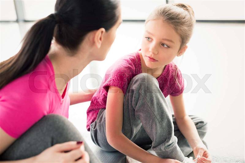 Mother and daughter in pink shirts sitting on floor in gym, stock photo