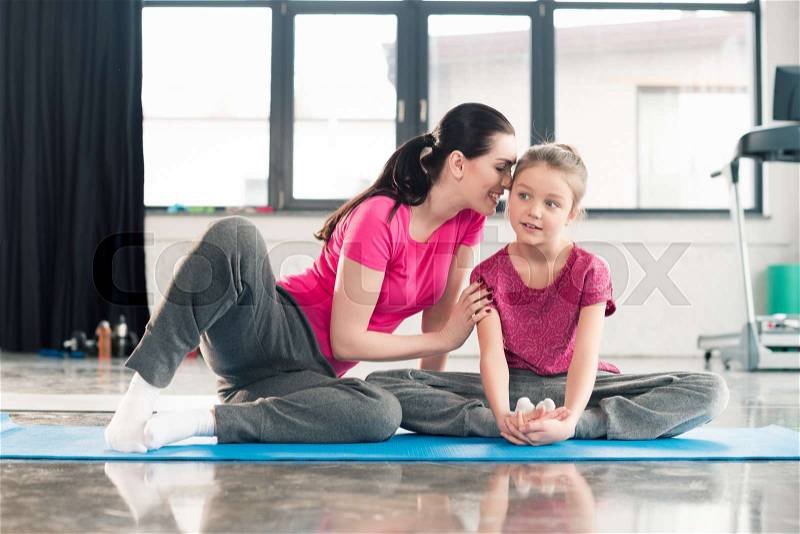 Mother and daughter in pink shirts sitting on yoga mat in gym , stock photo