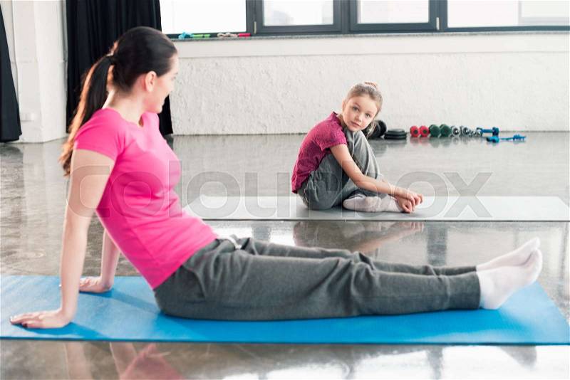Mother and daughter in pink shirts sitting on yoga mats in gym , stock photo