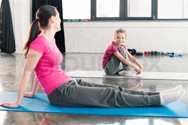 Mother and daughter in pink shirts sitting on yoga mats in gym , stock photo