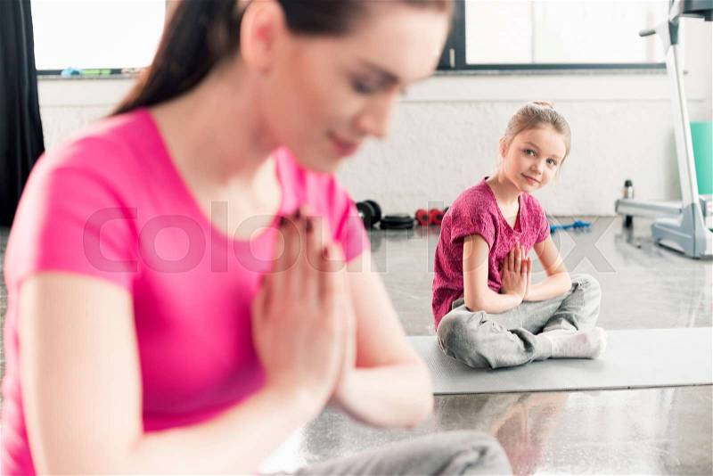 Mother and daughter in pink shirts sitting in lotos pose in gym, stock photo