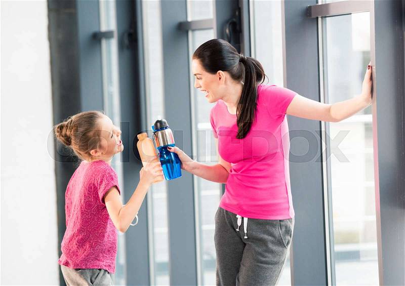 Mother and daughter in pink shirts with sport bottles in gym, stock photo