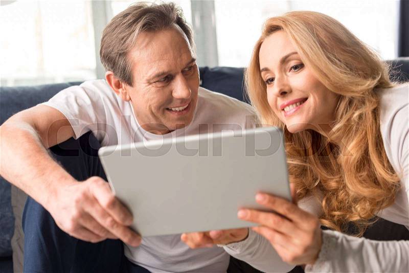 Happy middle aged couple using digital tablet at home , stock photo