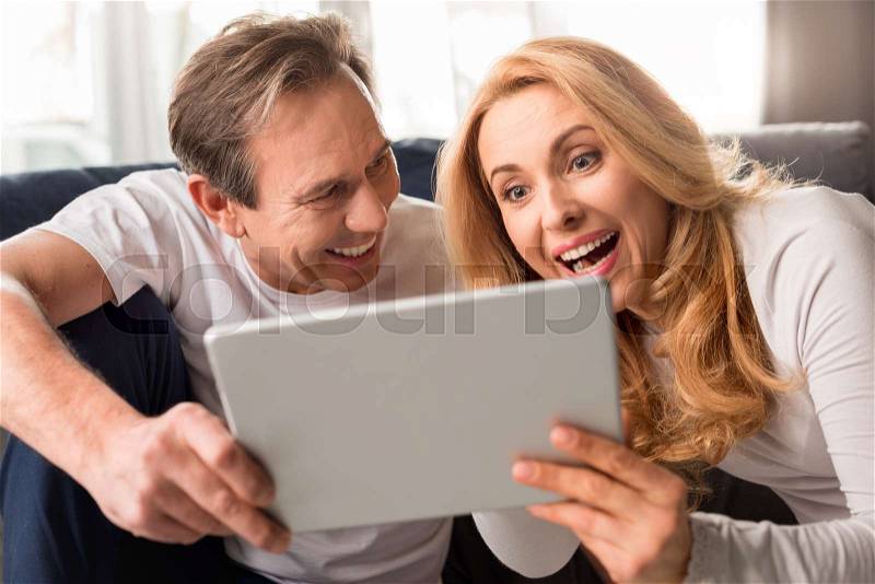Happy middle aged couple using digital tablet at home , stock photo