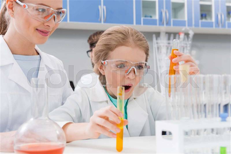Adult scientist and excited girl in goggles mixing reagents in tubes in laboratory, stock photo