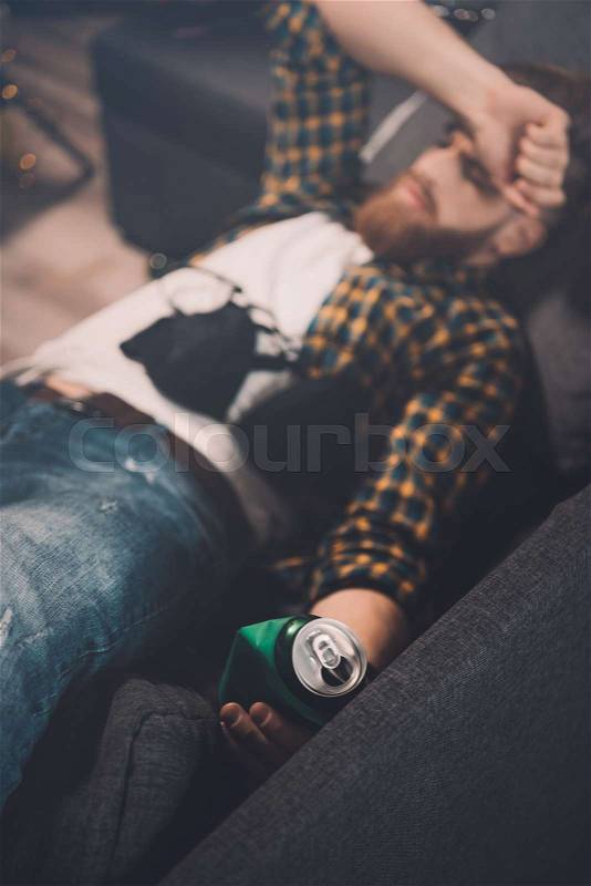 Drunk bearded young man sleeping on couch with bra and beer can after party , stock photo