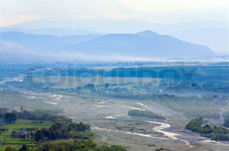 Misty summer countryside landscape with river and mountain behind, stock photo