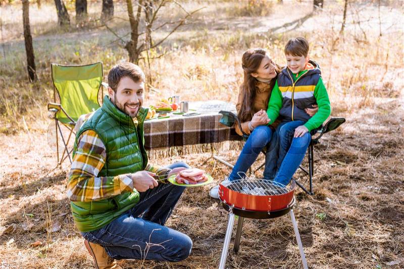Happy family grilling meat on barbecue grill in autumn park, stock photo