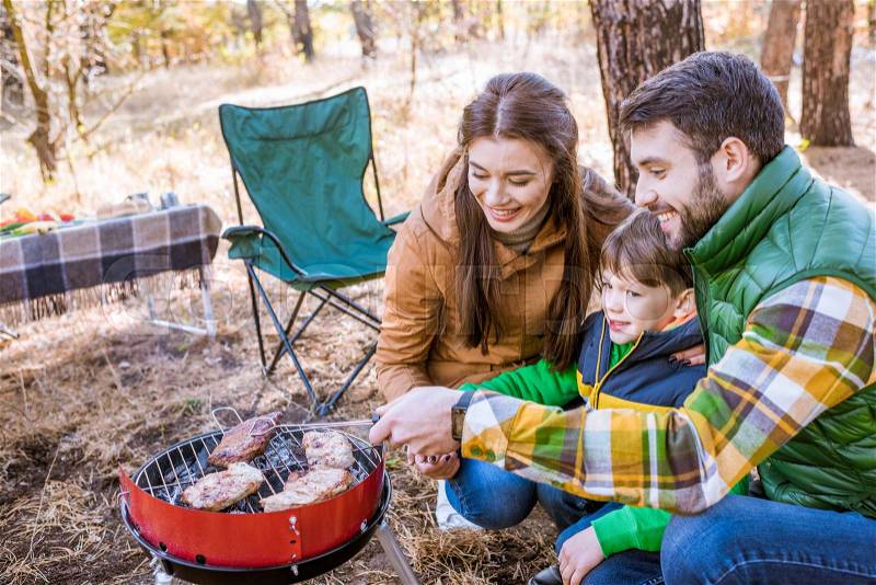 Close-up portrait of happy family grilling meat on barbecue grill in autumn park, stock photo