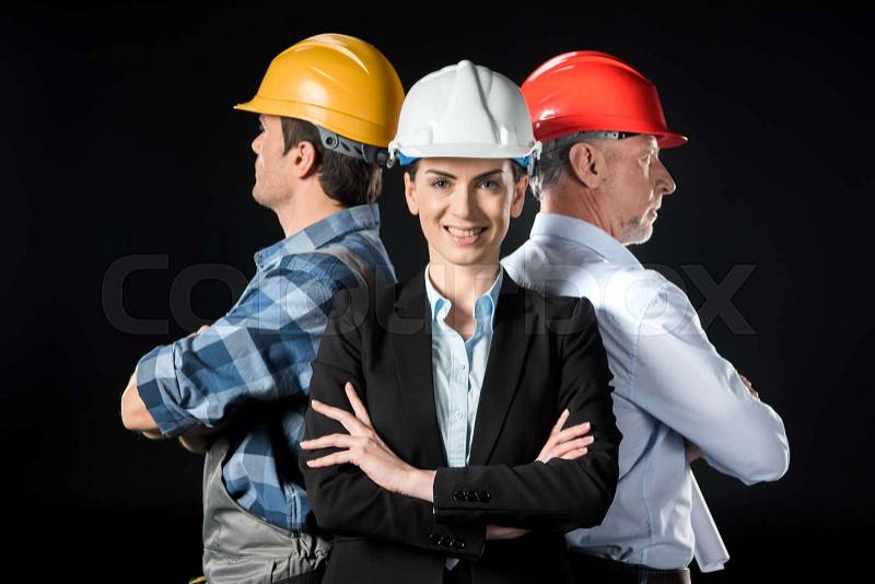 Portrait of two confident architects and engineer in hard hats on black, stock photo