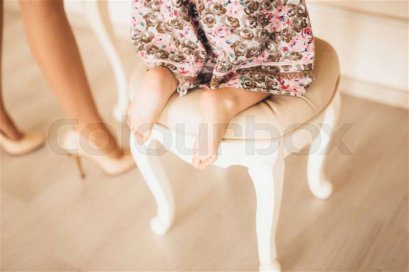 The legs of a child, a little girl in a chair in front of a mirror on the background of a wooden laminate, stock photo