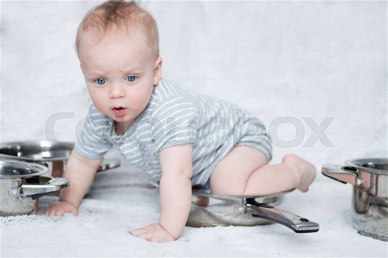 Mother\'s helper in a set of cooking pots and pans. Infant boy playing with a set of dishes. Cute toddler sitting on the frying pan, stock photo